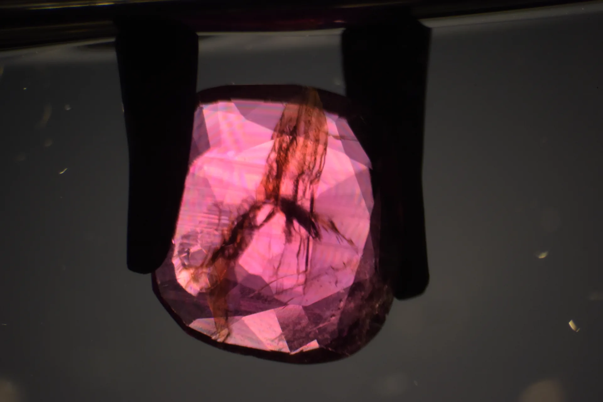 Rosa-violetter Korund von der Seite, Immersionsmikroskopie: brauner Federriss und regenbogenfarbige Streifen durch